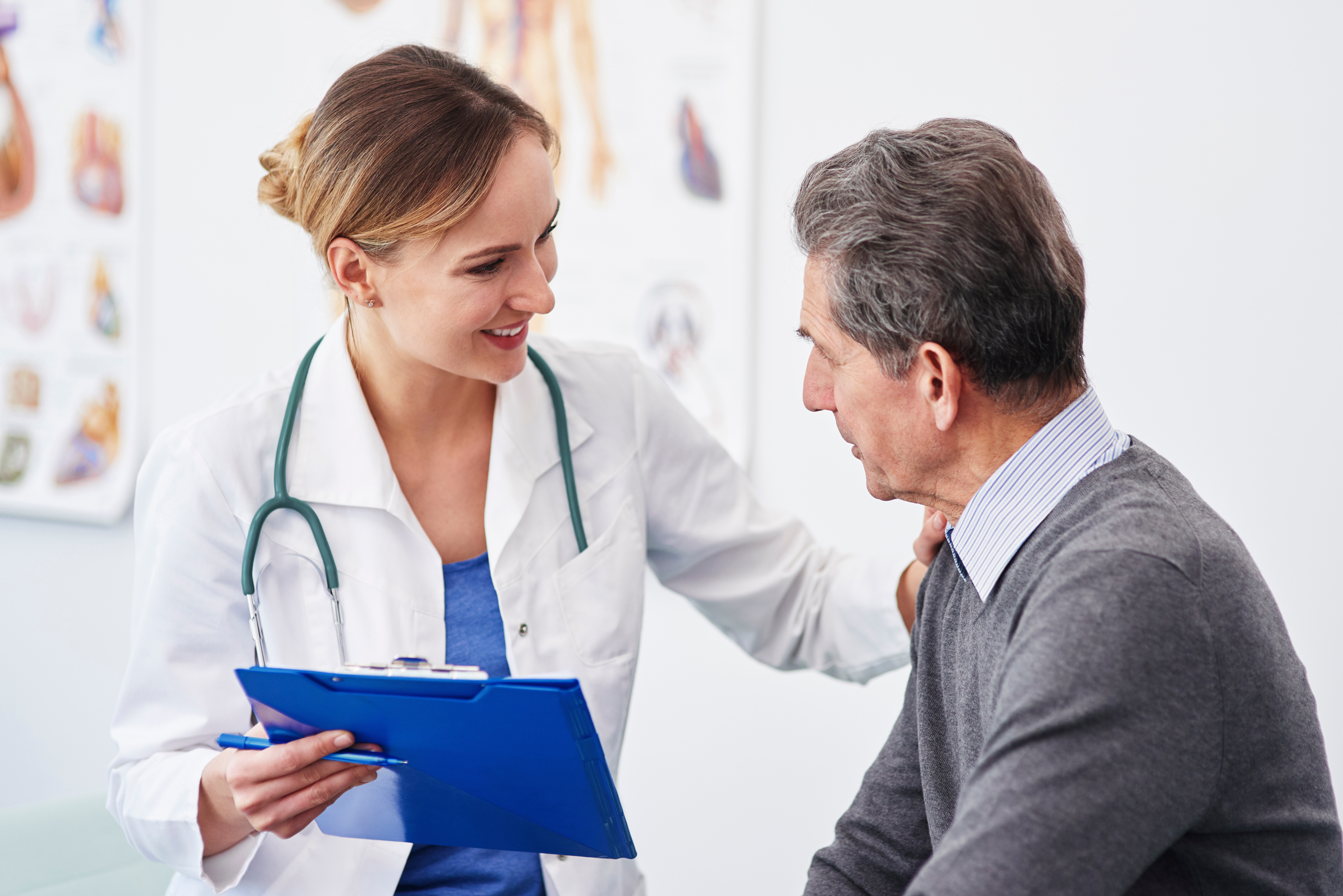 Physician consulting with an older male patient during a stroke care evaluation, holding a clipboard and discussing advanced treatment readiness