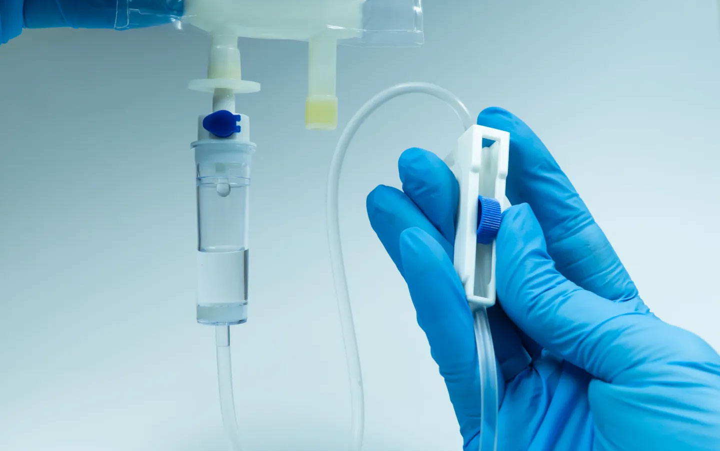 Gloved clinician adjusting an intravenous infusion set, illustrating medical device safety checks, functional performance testing, and regulatory compliance.
