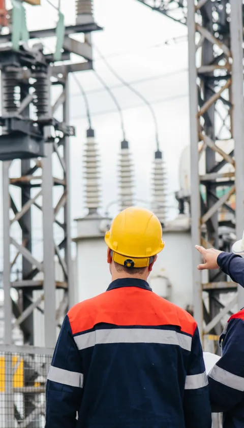 two workers in hard hats by electric grid facility